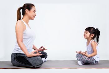 Young mother training lovely daughter with yoga