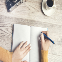 woman write in a notebook with cup of coffee and camera on table