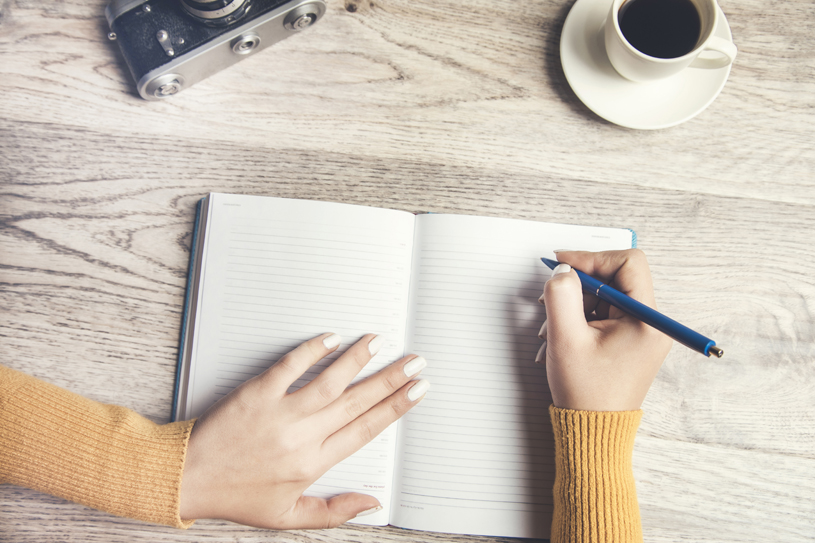 woman write in a notebook with cup of coffee and camera on table