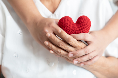 Young and senior woman holding each other hands and red yarn heart shape togetherness concept