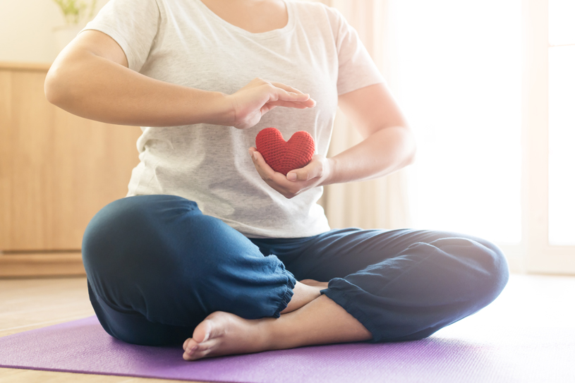 Woman hold red yarn heart shape in hand doing yoga post at home