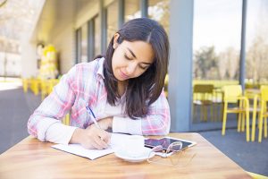 Focused young woman making notes in outdoor cafe