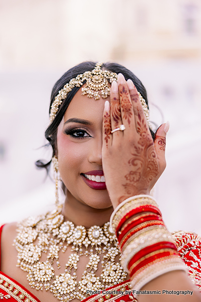 Kashmira in her bridal lehenga, adorned with intricate jewelry and henna, smiling gracefully.