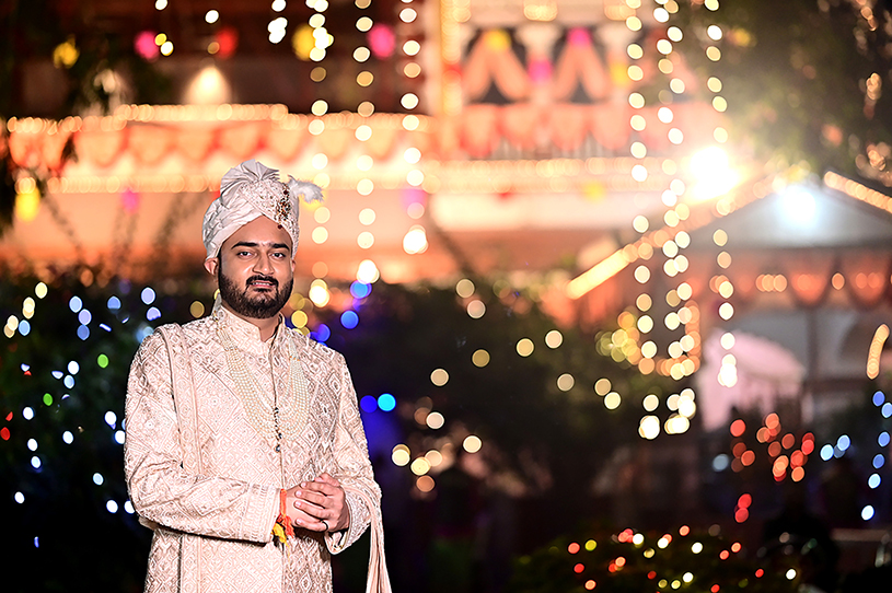 Groom Aneesh posing under festive lights at his Prayagraj wedding celebration