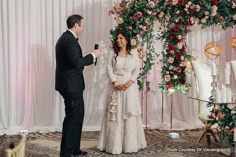 Sujata and Mark exchanging vows during their wedding ceremony under floral arch