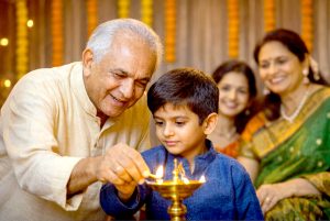 Grandfather teaching young boy to light traditional diya lamp during Indian family celebration while parents watch